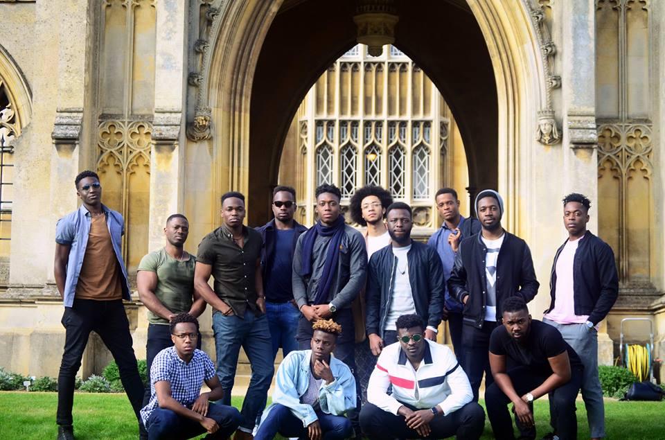 Fourteen black male students pose in front of the gates of St Johns College, Cambridge