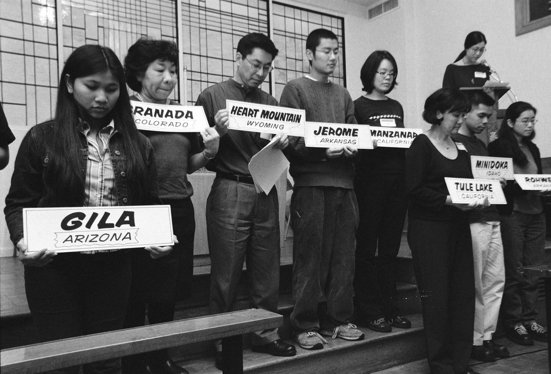black and white photo of people holding up signs of location names
