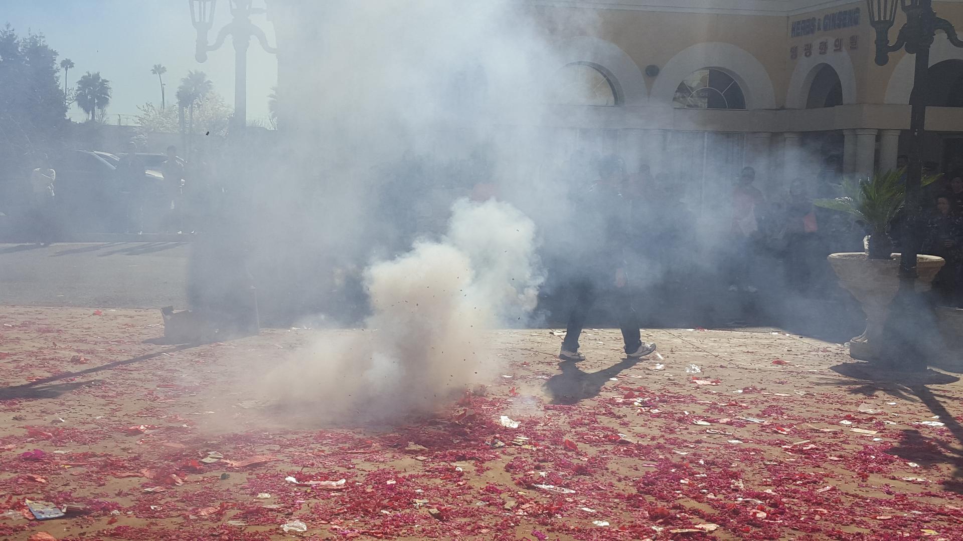 Smoke in front of a man, with remnants of firecrackers on the ground