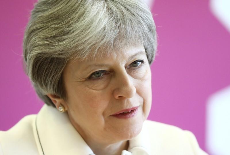 A portrait of British Prime Minister Theresa against a pink background. 