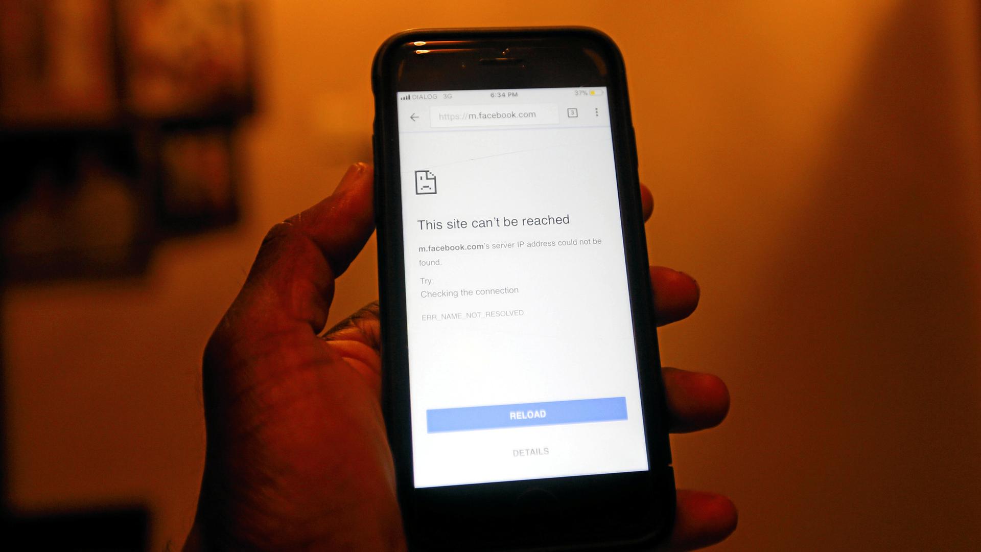 A hand holds a mobile phone with a Facebook logo and the message "this site cannot be reached."