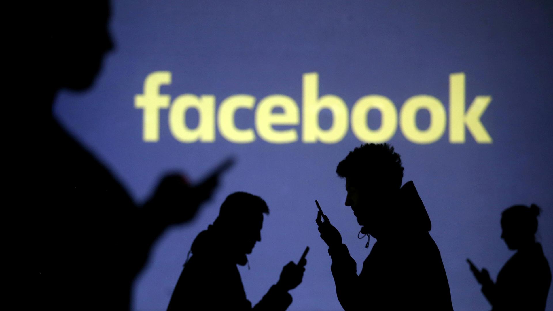 Silhouettes of people looking at their mobile phones in front of Facebook's logo. 