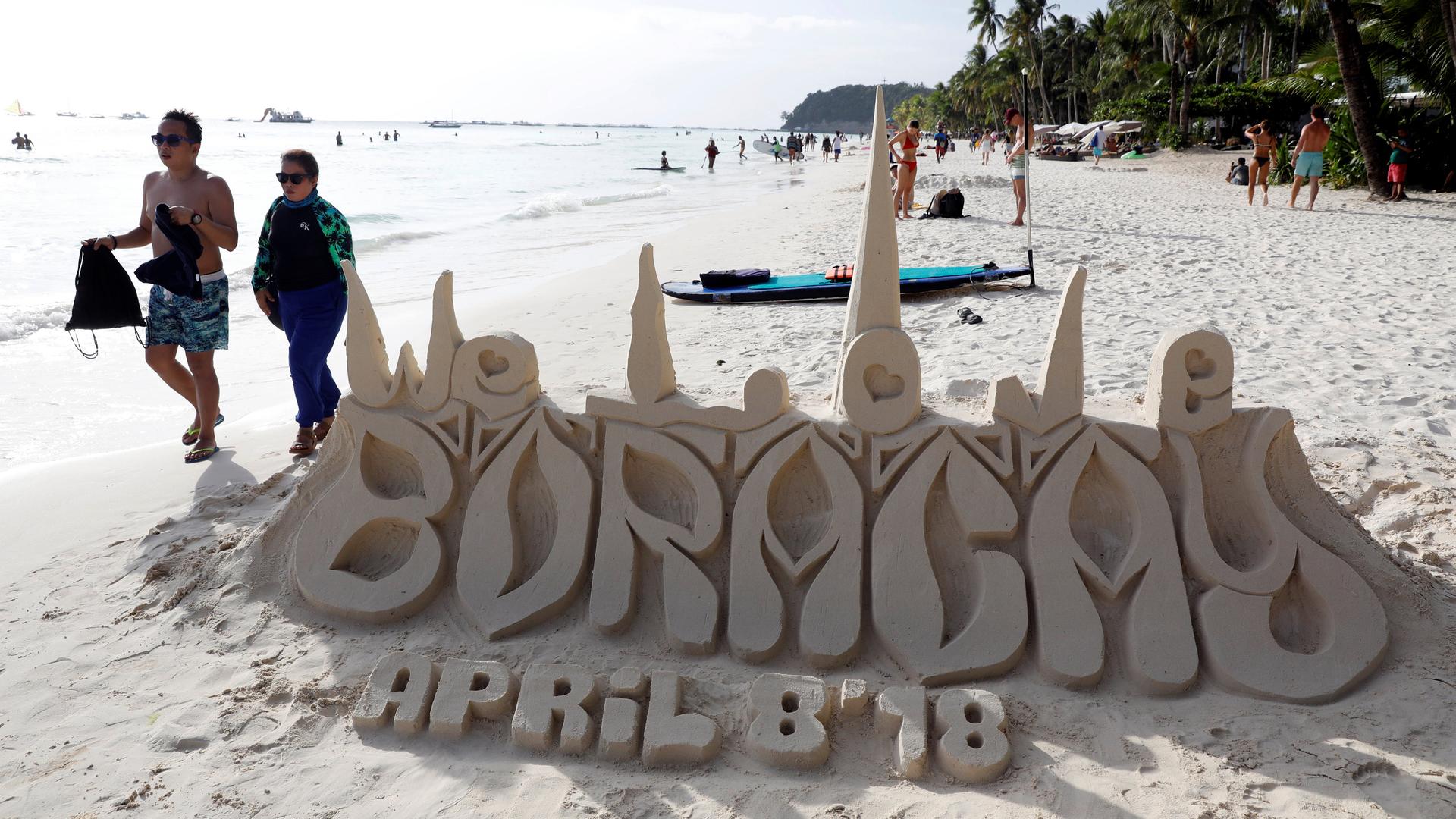 A sand sculpture reads Boracay April 8, 2018, as tourists wander by. 