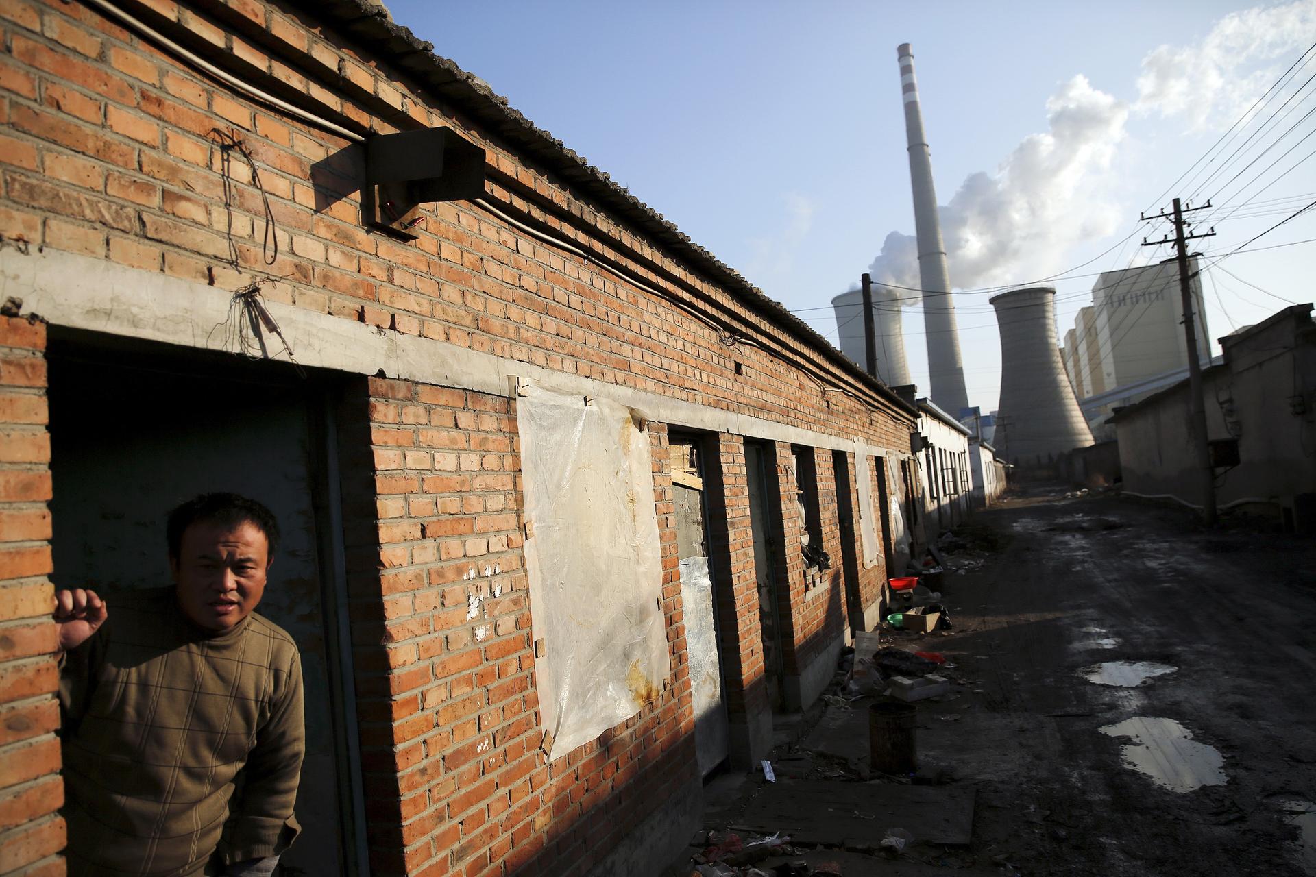 A man leans out of the door of his house down the street from large coal power plant smokestacks in Beijing.