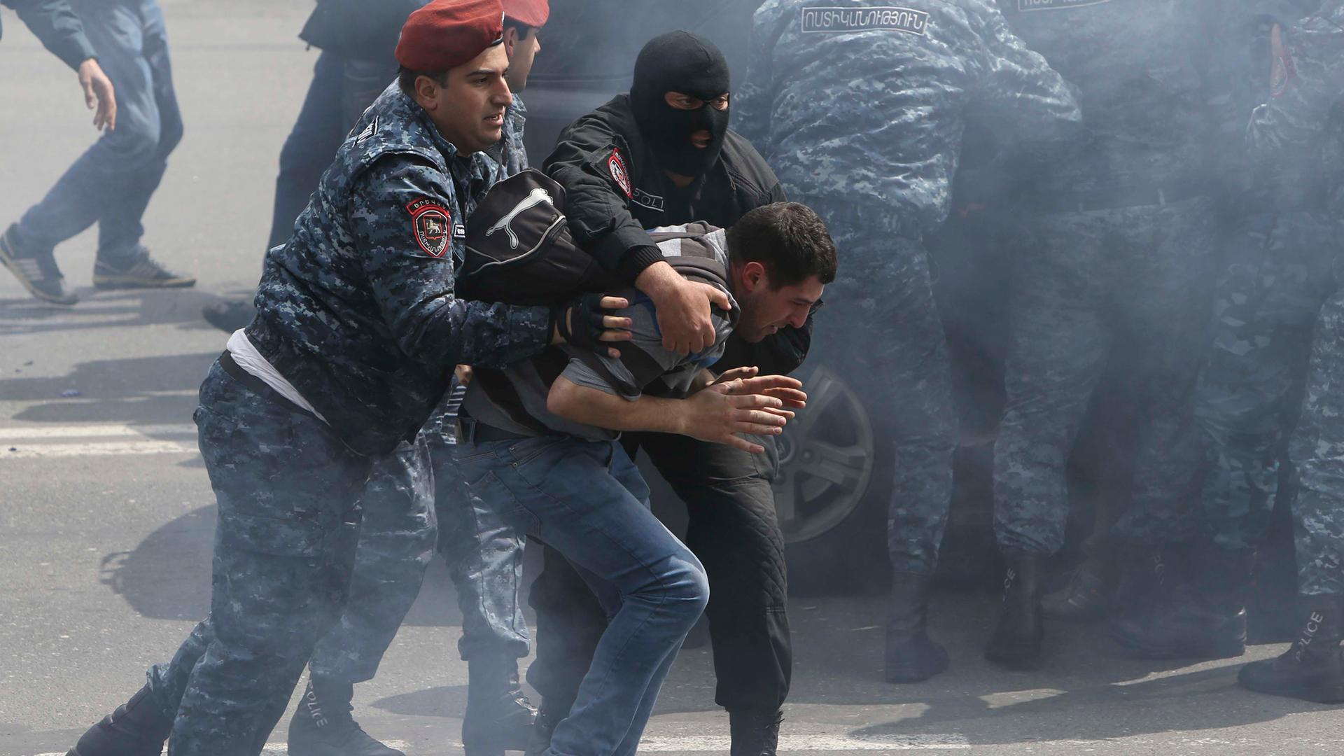 Red beret-wearing Armenian law enforcement officers detain a man during a protest.
