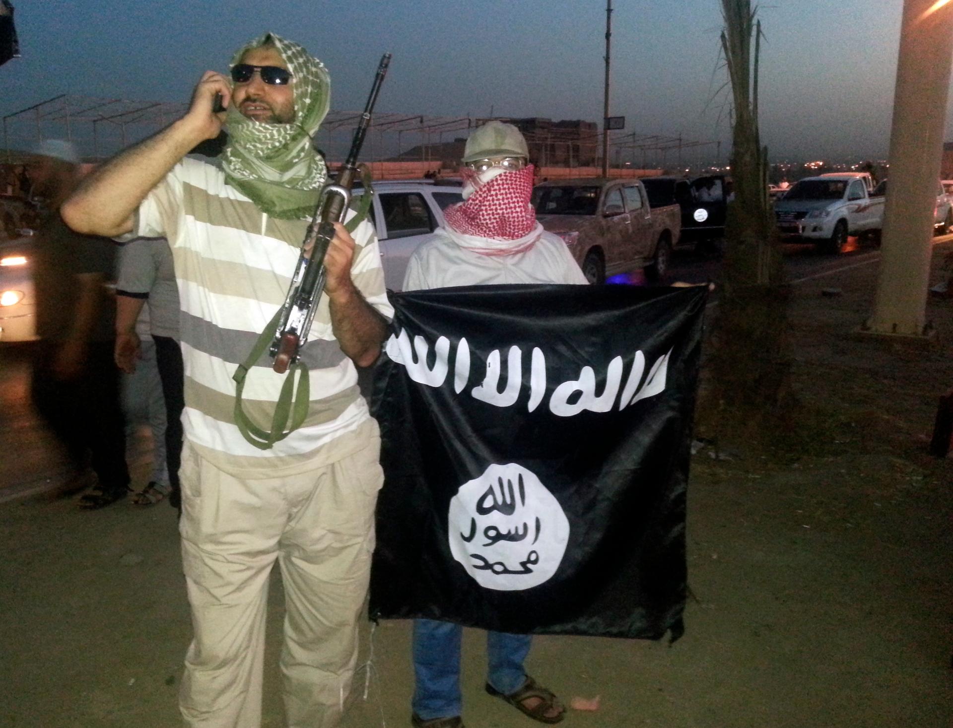 A fighter of the Islamic State of Iraq and the Levant (ISIL) holds a weapon while another holds a flag in the city of Mosul, shortly after the Islamic State captured the city. The flag reads, "There is no God but God, and Muhammad is the Messenger of God.