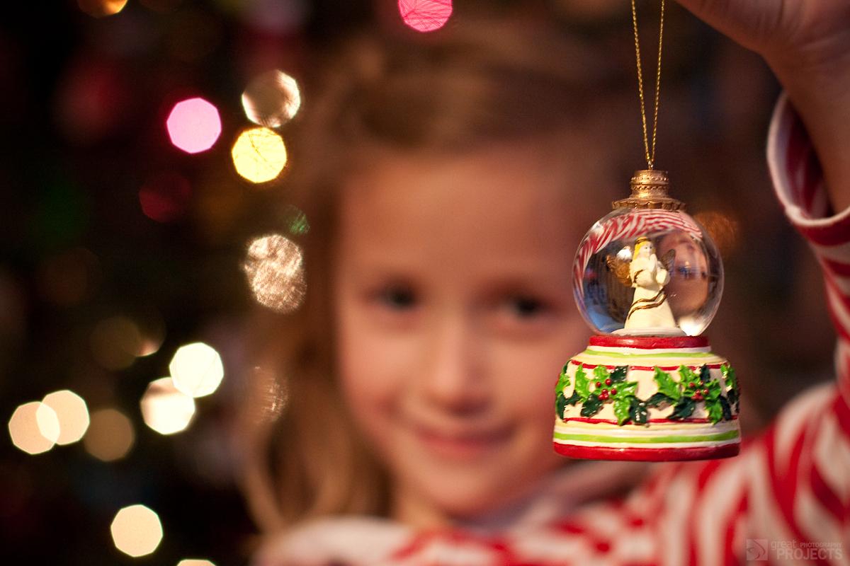 A girl holds a snowglobe Christmas ornament in front of her family's tree. Some non-Christian families have adopted trees and other Christmas traditions.