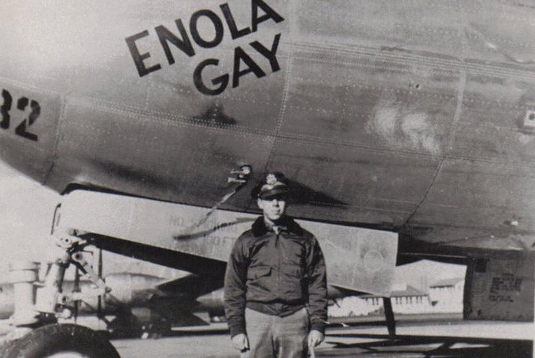 A uniformed man stands in front of the bomber Enola Gay