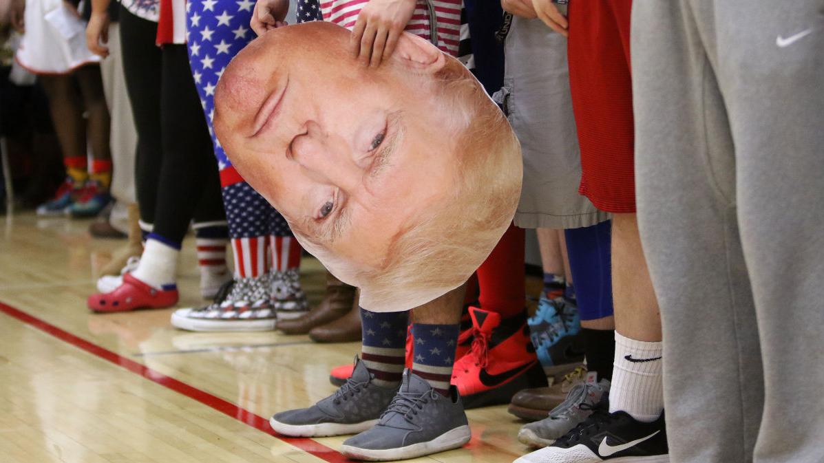 Fans legs, one holding a large poster of Trump's face