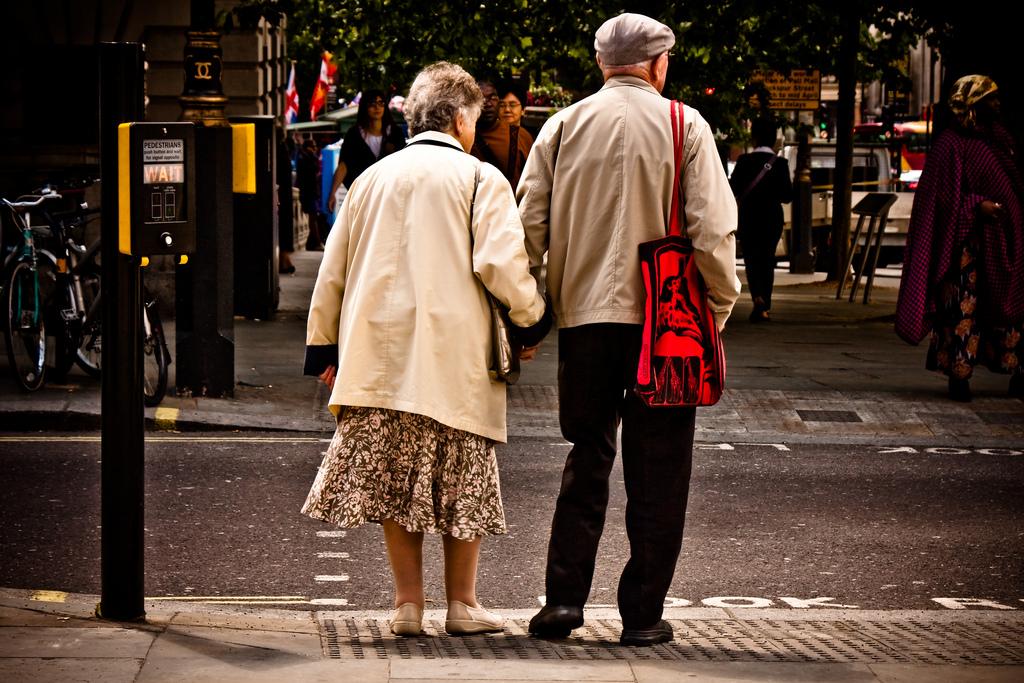 An elderly couple holds hands while waiting to cross a London street.