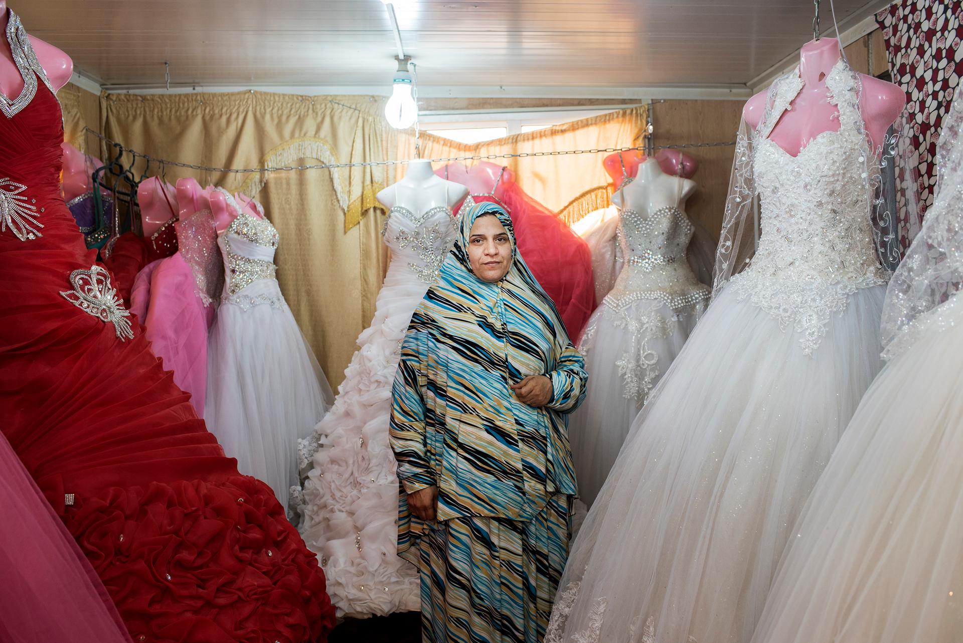 Um Mohammed, a Syrian refugee hailing from the southern Daraa region, stands in her wedding dress shop in Jordan's Zaatari camp. Expecting another child, Um Mohammed said she opened the shop a year and a half ago to help generate extra income for her grow
