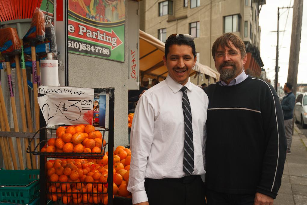 Two men in smile in posed photo in front of small market