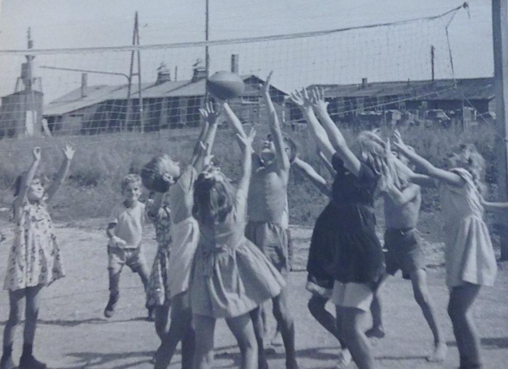 A group of children jump and reach for a ball on a volleyball court at a refugee camp in Germany after World War II