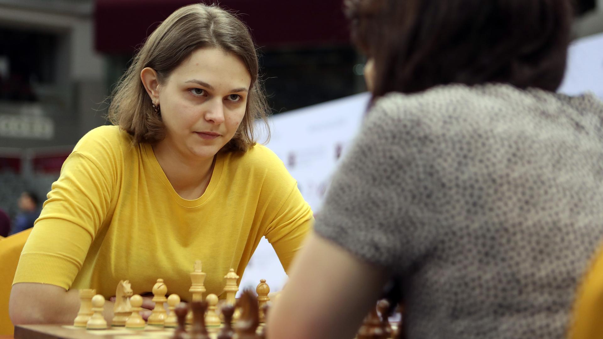 Ukraine's grandmaster Anna Muzychuk, wearing a yellow shirt, stares down her opponent across a chess board.