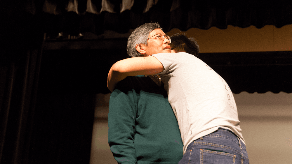 A man is hugged by a young man on stage