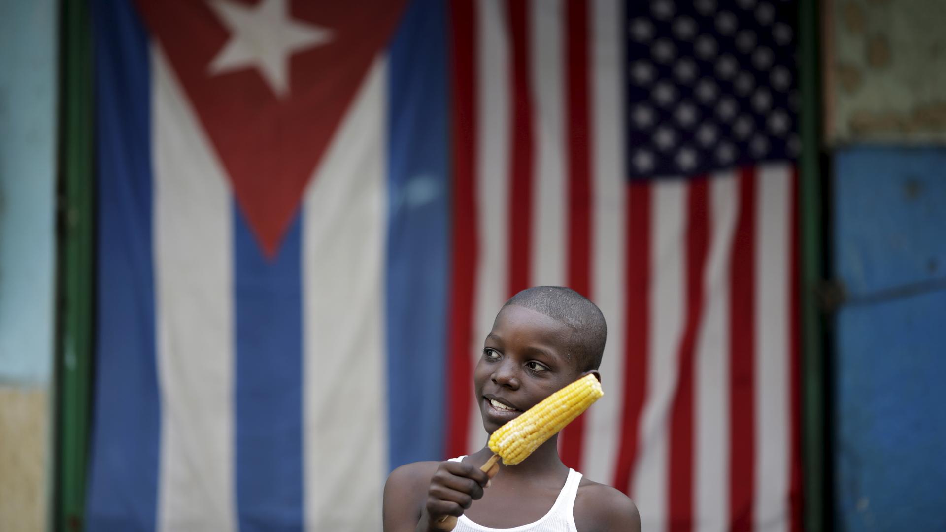 Jimmy Blanco, 9, holds a corncob in front of the Cuban and the U.S. flags in Havana, March 23, 2016. Struggling under a US embargo, many Cubans hope an easing of US-Cuban trade relations will bring material improvements to their lives.