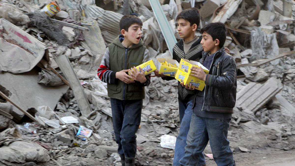 Boys carry boxes of biscuits near rubble of damaged buildings in Aleppo, March 2, 2016.
