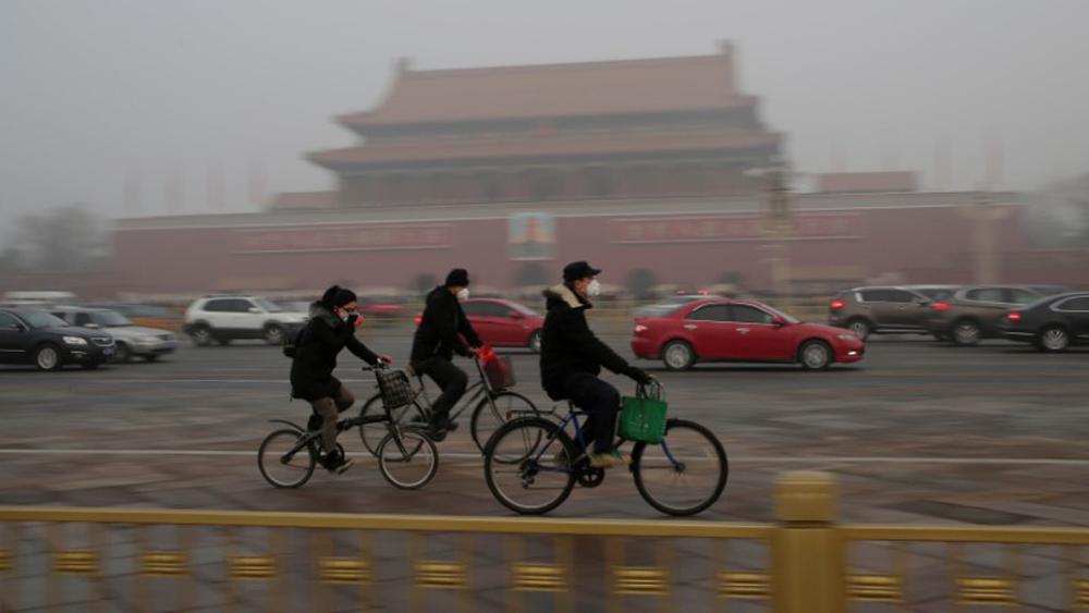 Three bicyclists wearing face masks ride past Tiananmen Gate.