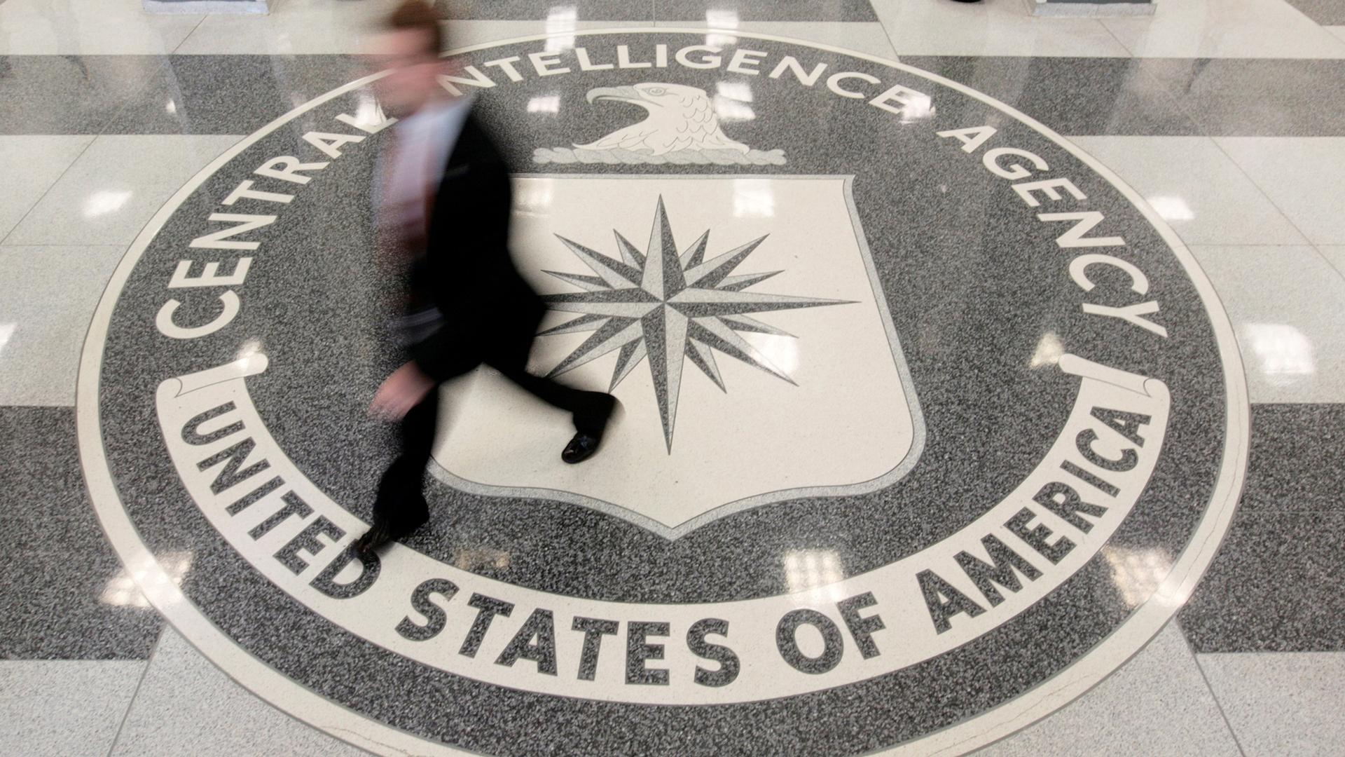 A man in a suit walk over the seal of the CIA at CIA headquarters.