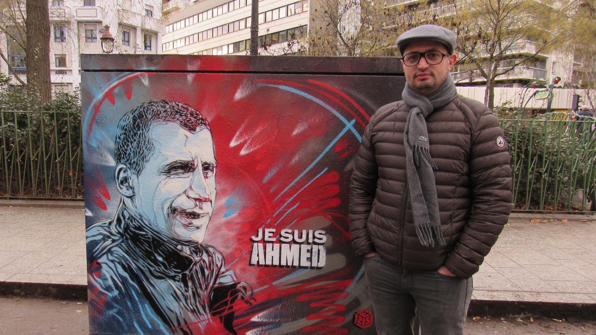 Djamel Adane next to a portrait of Ahmed Merabet, the police officer killed the day of the Charlie Hebdo attacks. Adane was there, and he held Merabet's hand while they waiting for the ambulance to arrive.
