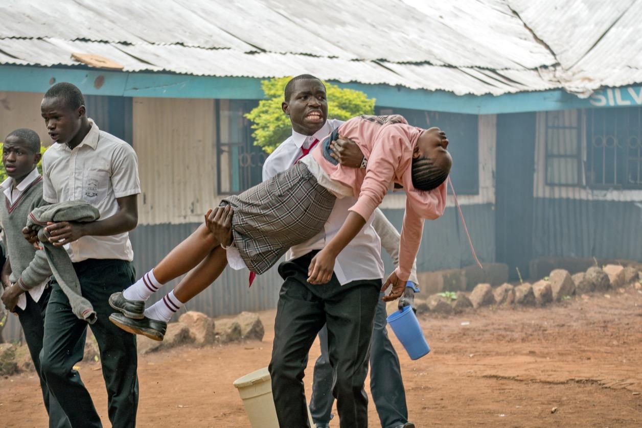A student carries his classmate out of the Silver Spring Secondary School in Nairobi, Kenya, after she collapsed inside her classroom.