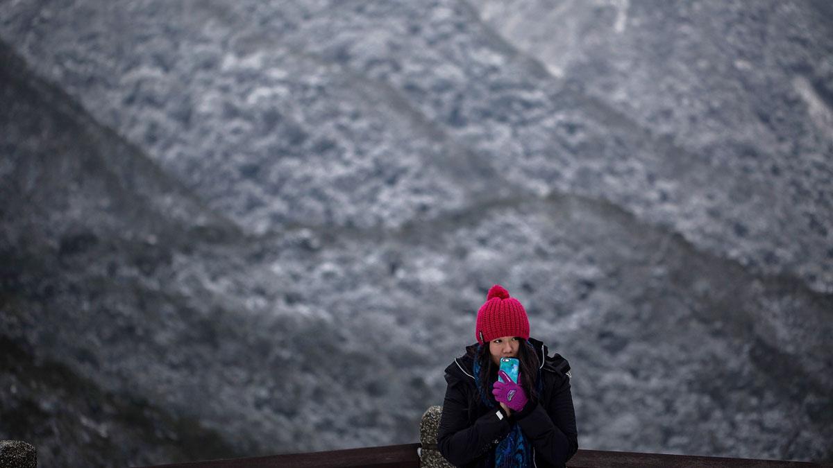  A woman takes photographs as snow is seen at the background on the Yangmungshan National Park during a snowfall in Taipei, Taiwan. Taiwan experienced a sudden drop in temperature over the weekend.