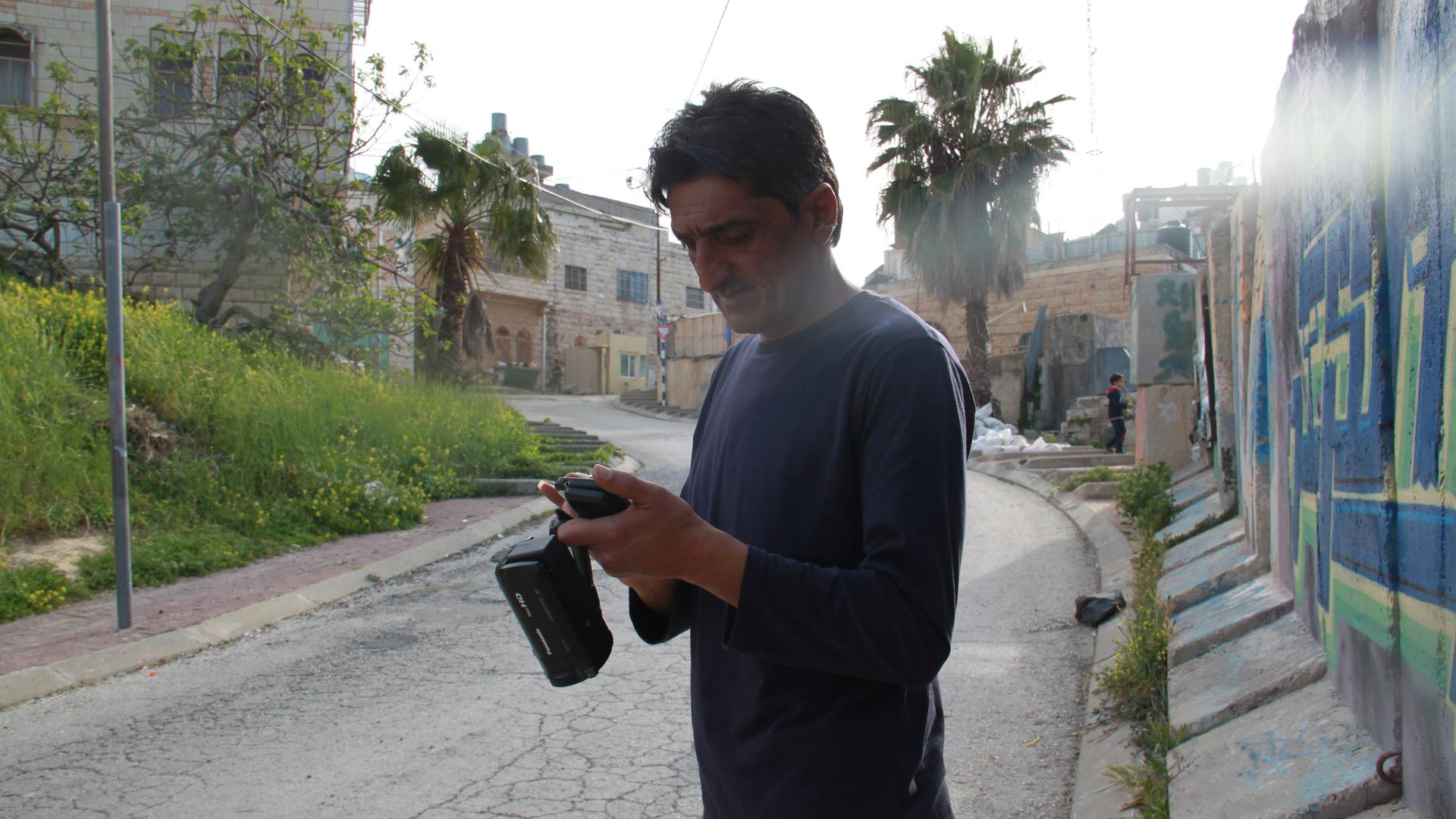 Emad Abu Shamsiyeh who filmed the shooting, standing with his camera at the site in Hebron where it happened. Since his video was posted online, he's been threatened and attacked.