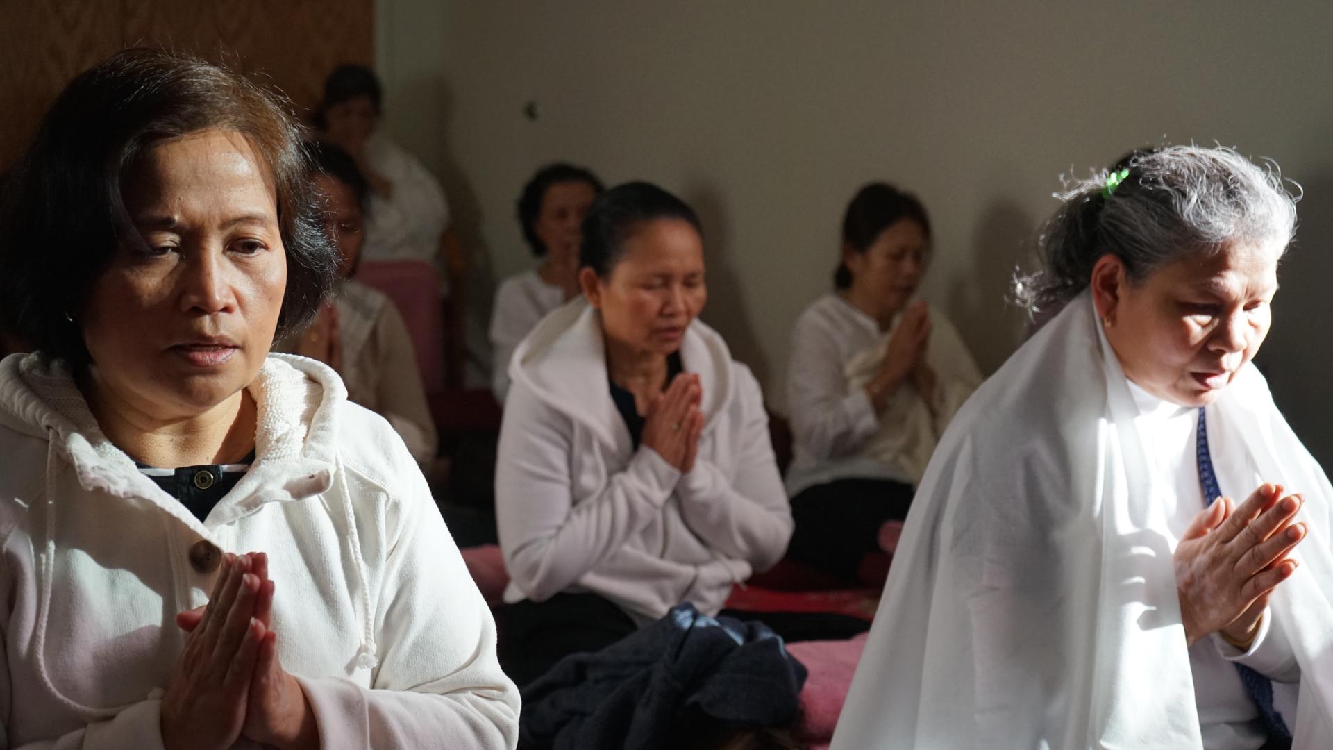 Cambodian women meditating in the Metta Center's meditation lounge, sitting cross-legged with palms pressed together