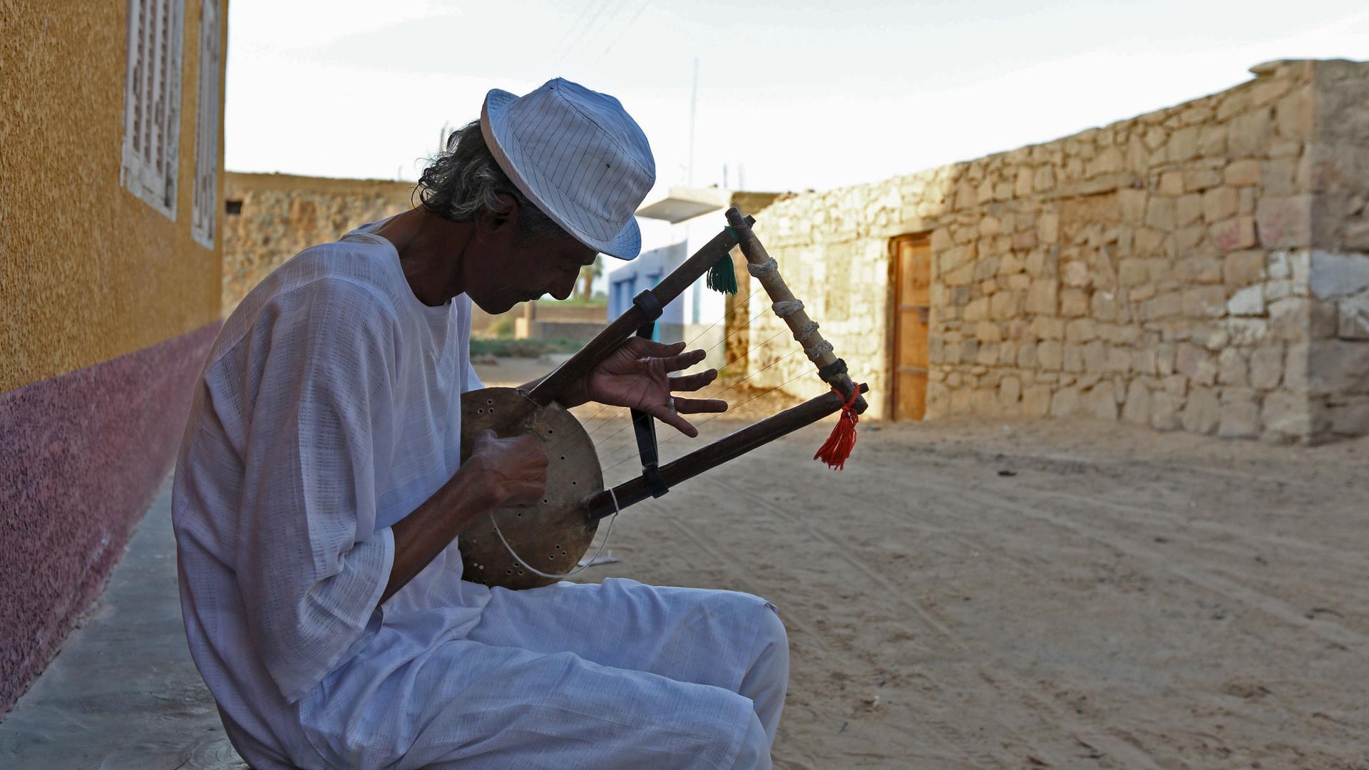 A man plays music on a traditional musical instrument in the Nubian village of Adindan