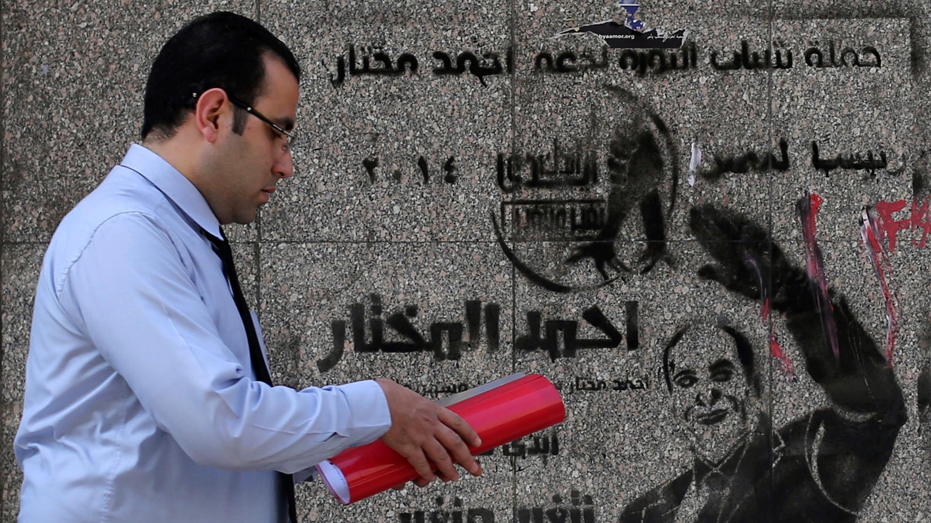 A man walks past a wall graffiti regarding the 2014 presidential election in downtown Cairo, February 25, 2014. The graffiti reads: "Ahmed Al Mukhtar - President of Egypt, Your hand with my hand, we can change our country."