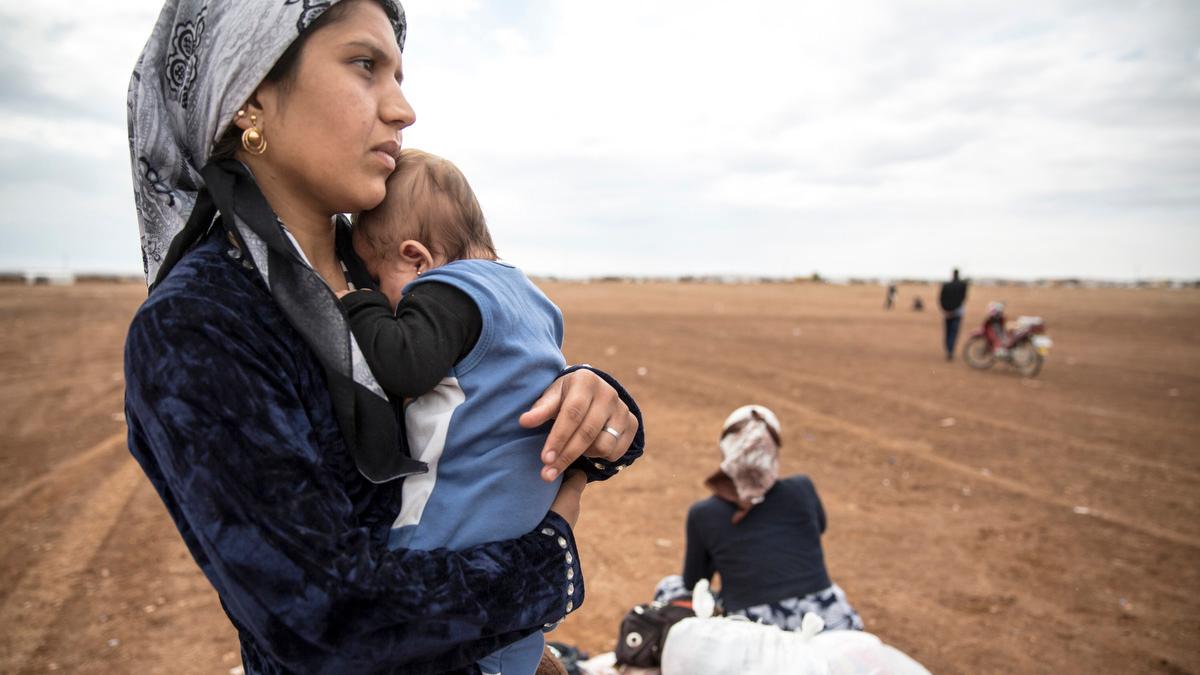 A Syrian woman holding her infant waits near an informal border crossing to go back to Kobane, Syria, despite ongoing clashes between ISIS and Kurdish fighters. Many Syrian Kurds are finding Turkey expensive and inhospitable.