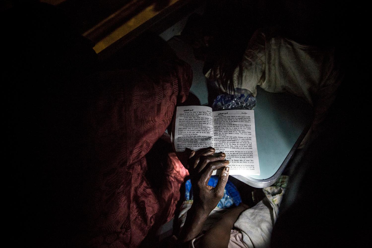 On a train home from Lagos to Kano, a Hausa woman reads a romance novel with the flashlight of her phone.