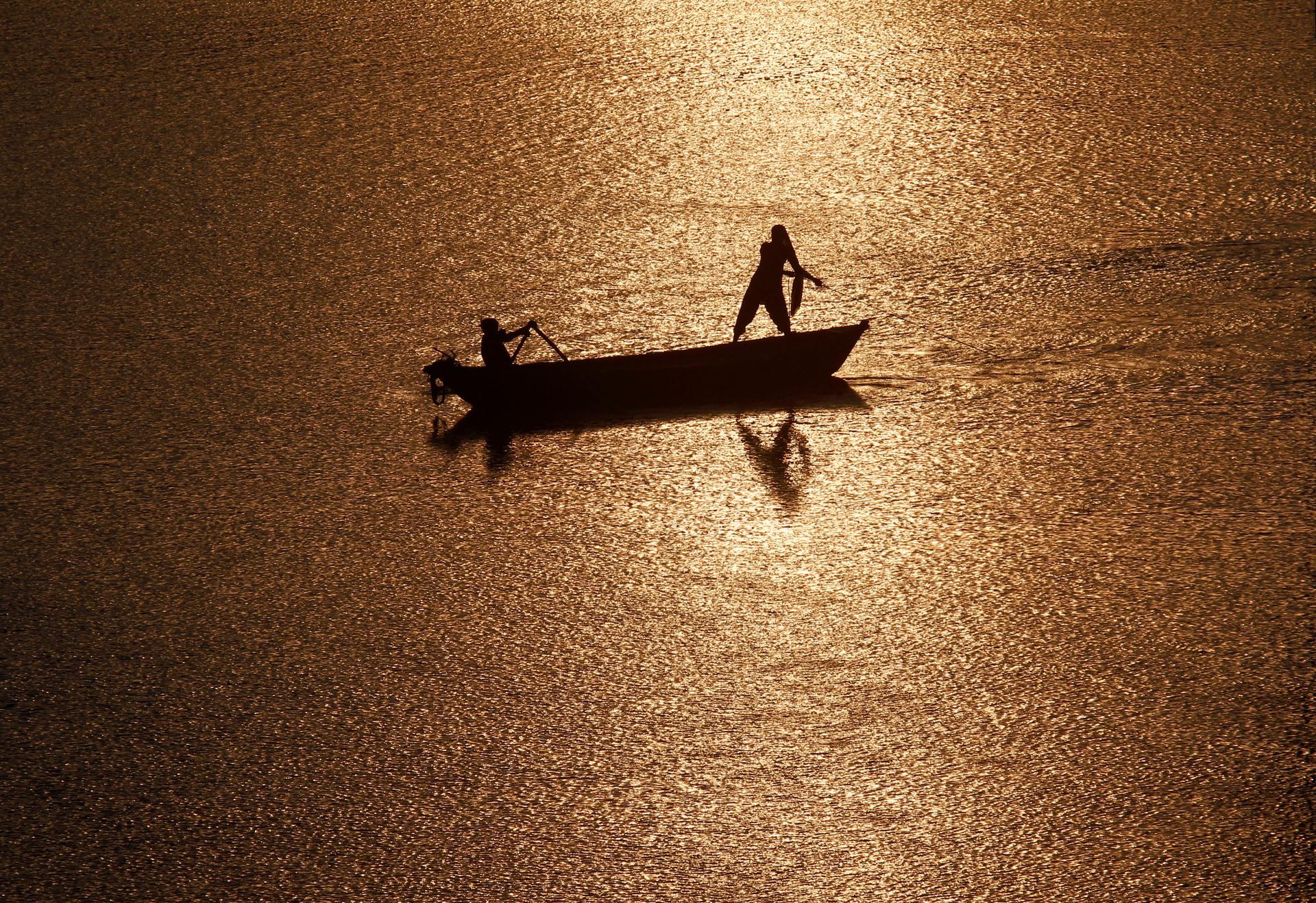 Fisherman are silhouetted against the rising sun in the waters of the Ganges river.
