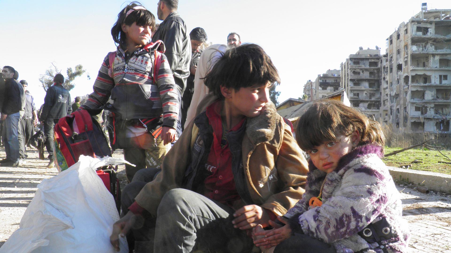Children sit with their belongings as they wait to be evacuated from a besieged area of Homs February 12, 2014. 