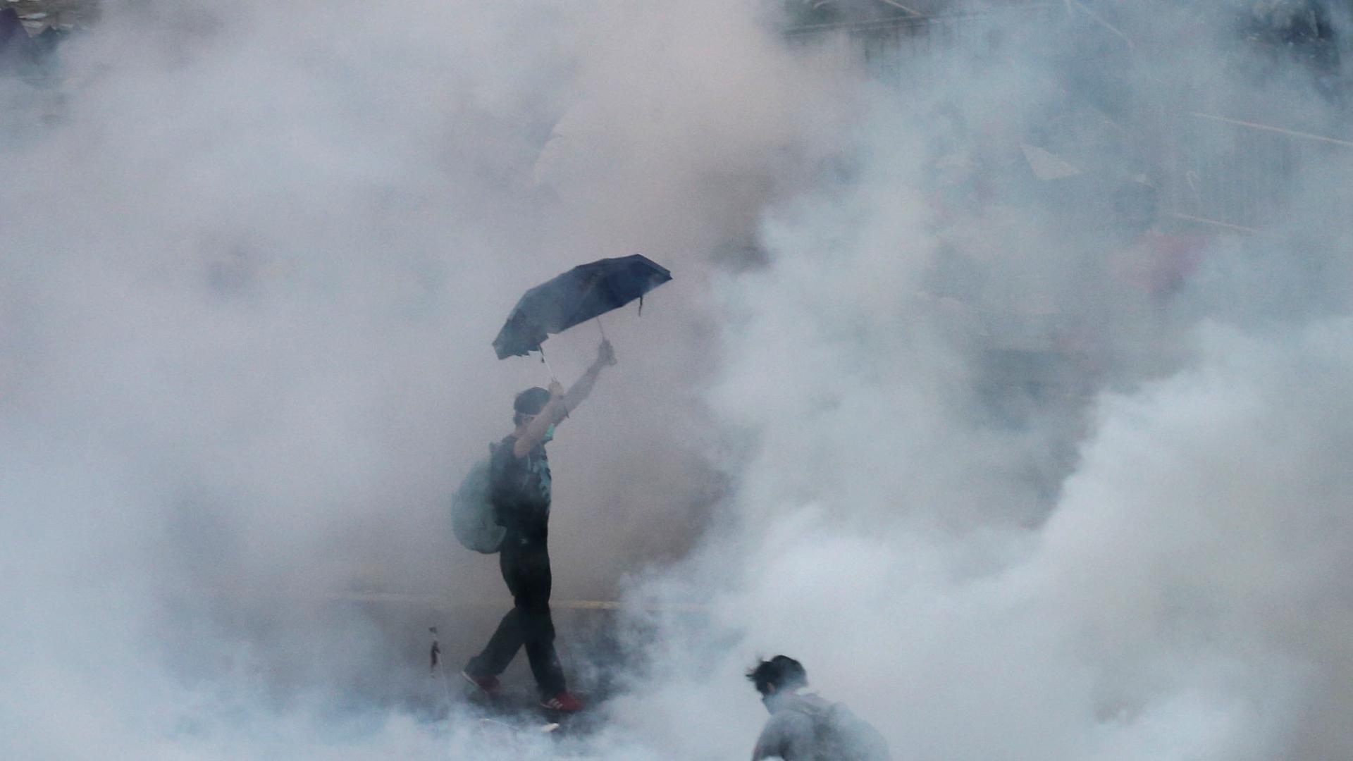 A protester walks in tear gas fired by riot policemen after thousands of protesters blocked the main street to the financial district outside government headquarters in Hong Kong on September 28, 2014. 