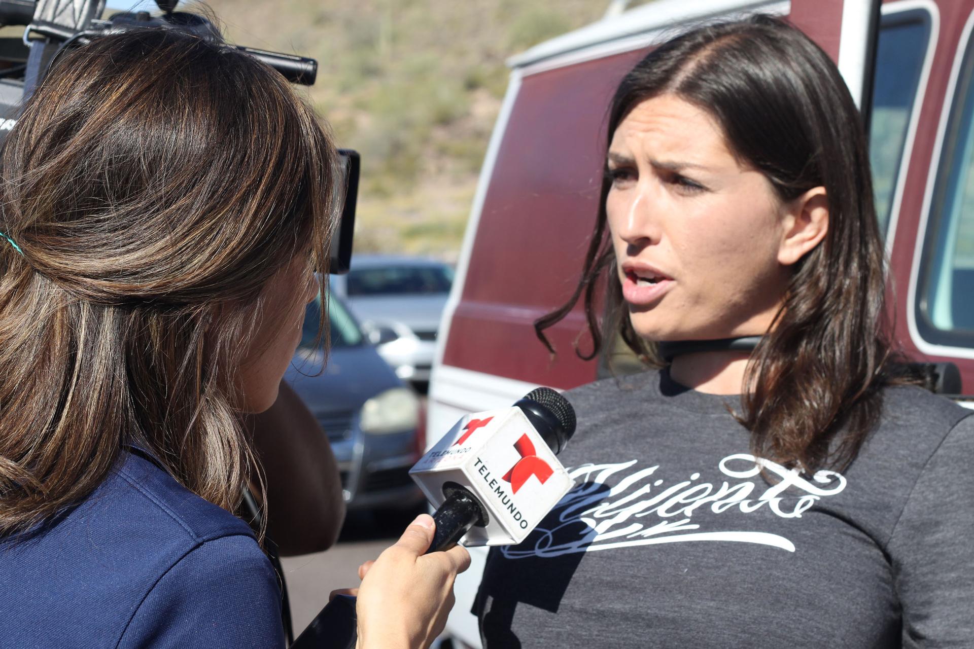 Gonzalez locked to a vehicle with a chain around her neck, being interview by a reporter.