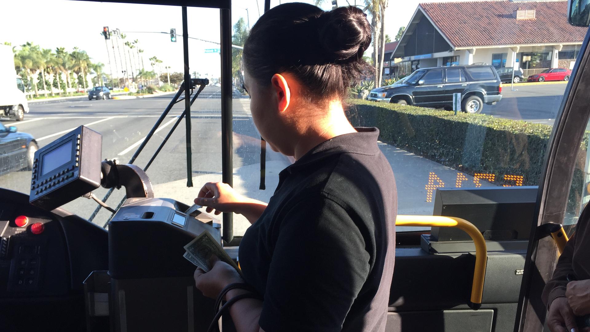 Woman putting bills in public bus machine, with windshield behind her