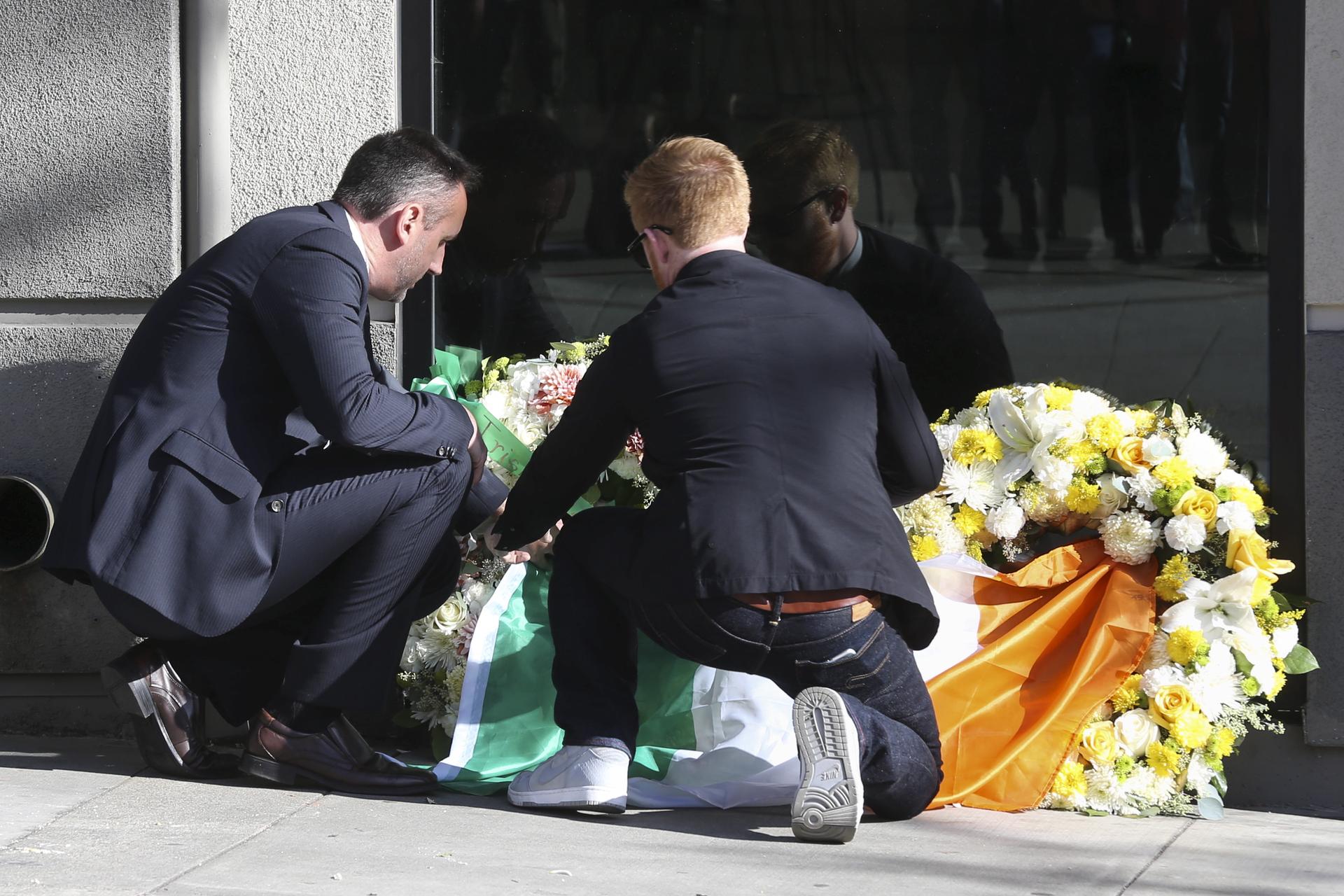 Philip Grant, Consul General of Ireland to the Western United States (L) helps Neil Sands, President of the Irish Network Bay Area, lay an Irish flag atop two wreaths at the scene of a 4th-story apartment building balcony collapse in Berkeley, California.