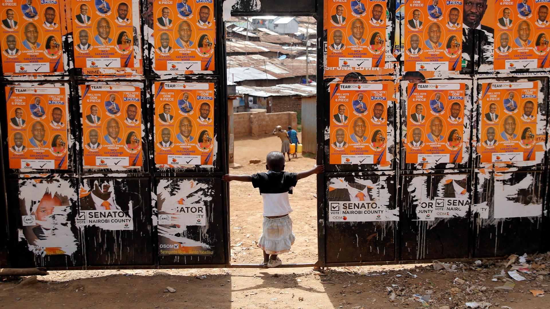 A child plays at the entrance of a polling station pasted with campaign posters ahead of the presidential election in the Kibera slums of Nairobi, Kenya.