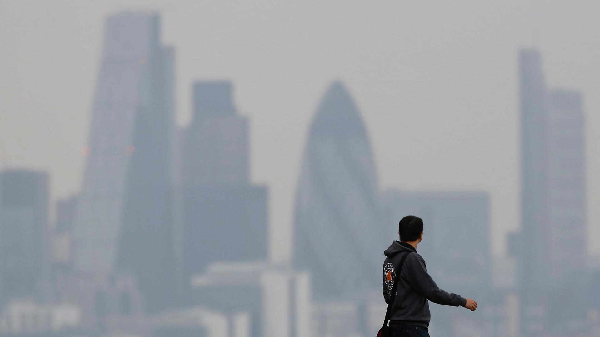 A man walks through Greenwich Park as a haze of pollution sits over the London skyline.
