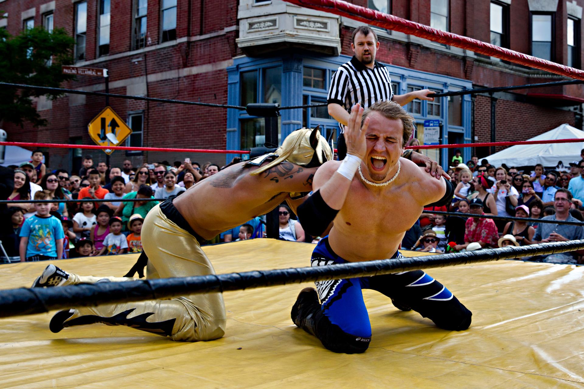 Man in wrestling ring being tackled with referee in background