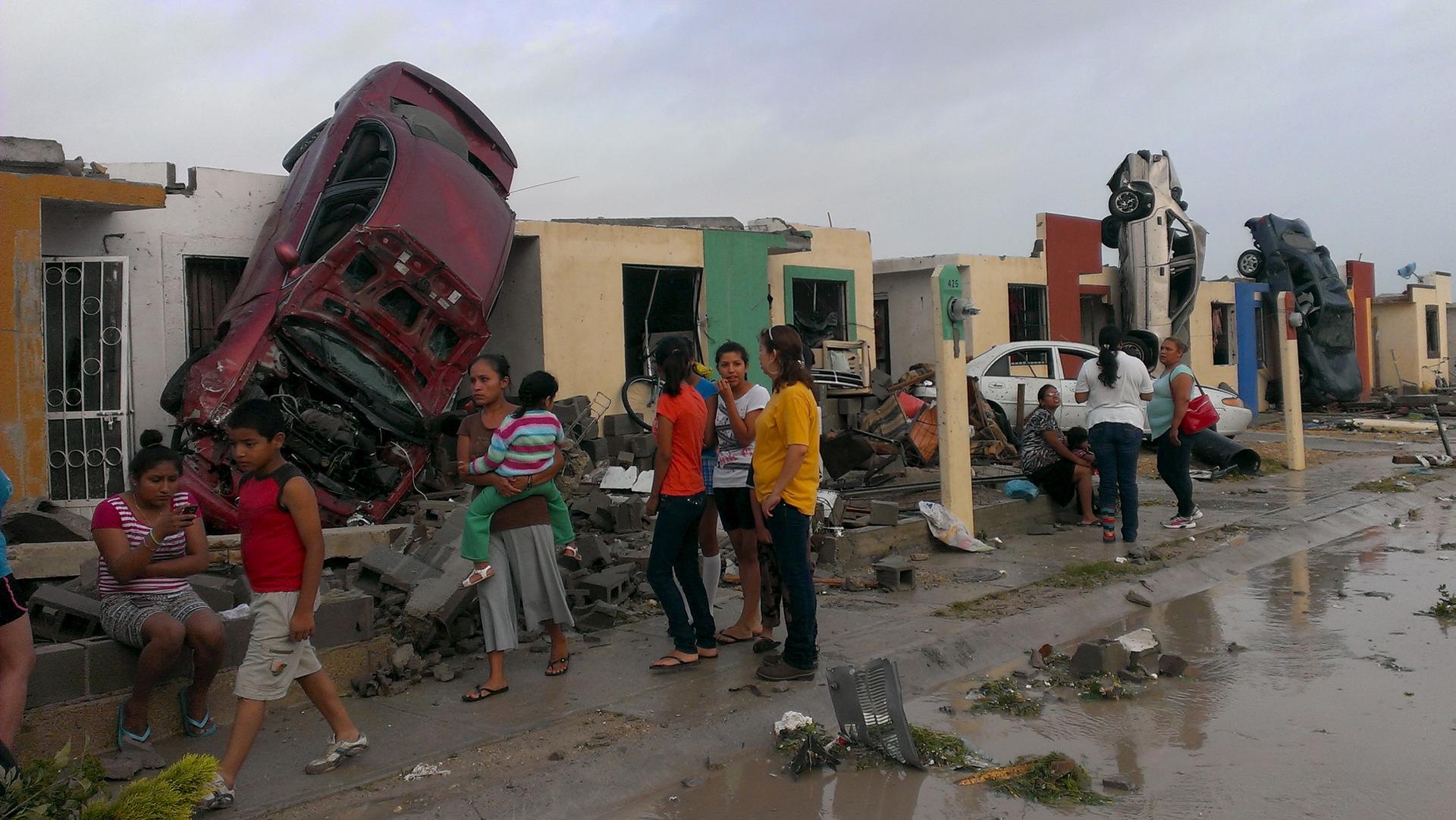 Residents stand outside their homes as damaged cars are seen after a tornado hit the town of Ciudad Acuña, state of Coahuila.