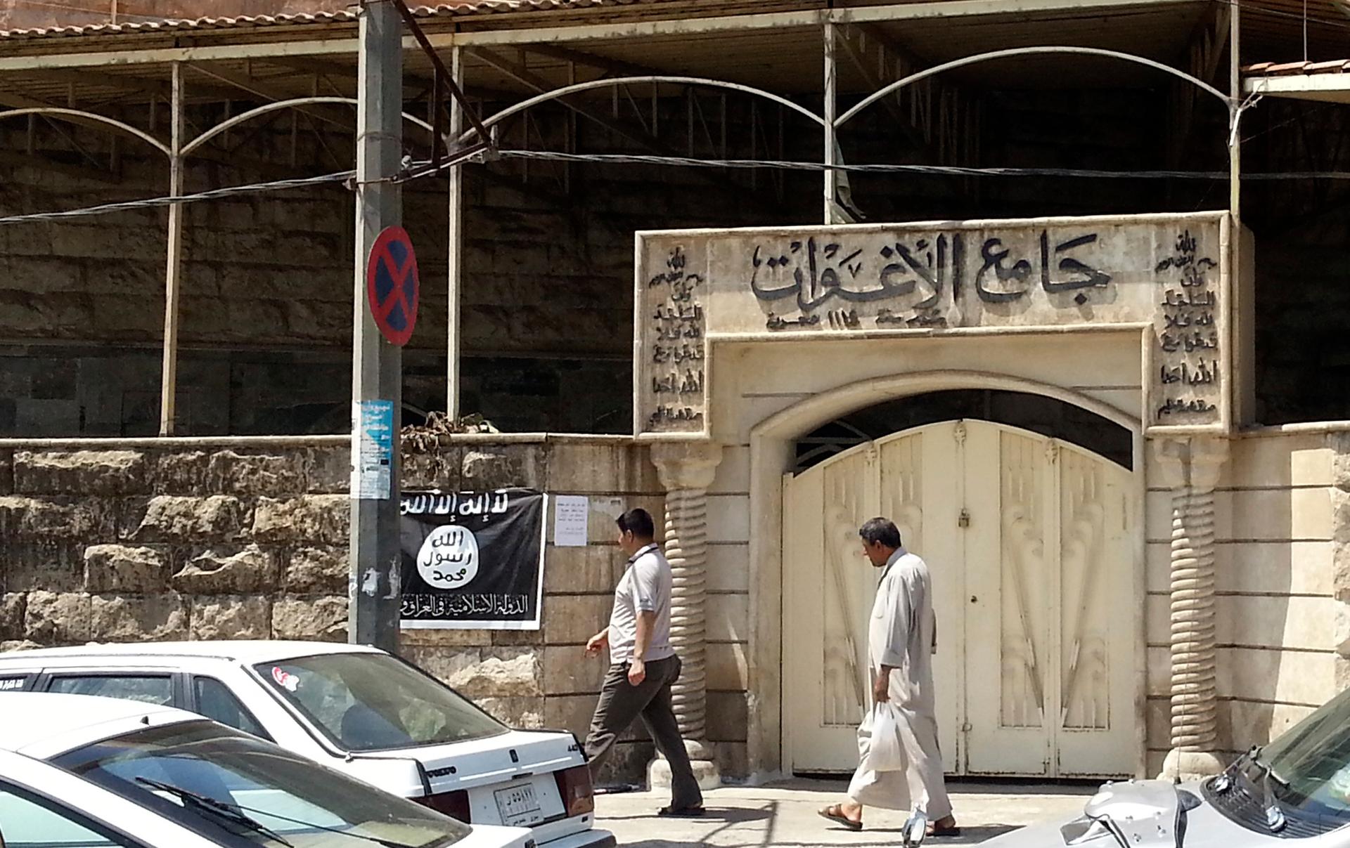 People in Mosul walk past a flag for Islamic State in Iraq and Syria