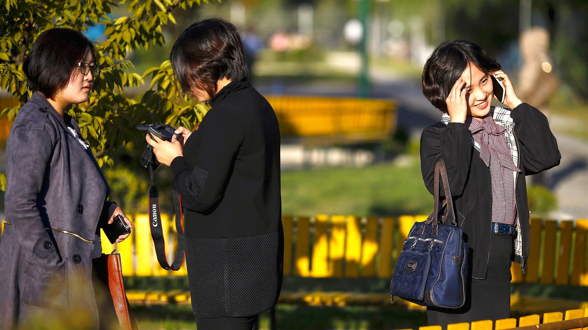 North Koreans chat on mobile phones and take some pictures as they enjoy nice weather in a park in central Pyongyang on October 11, 2015.