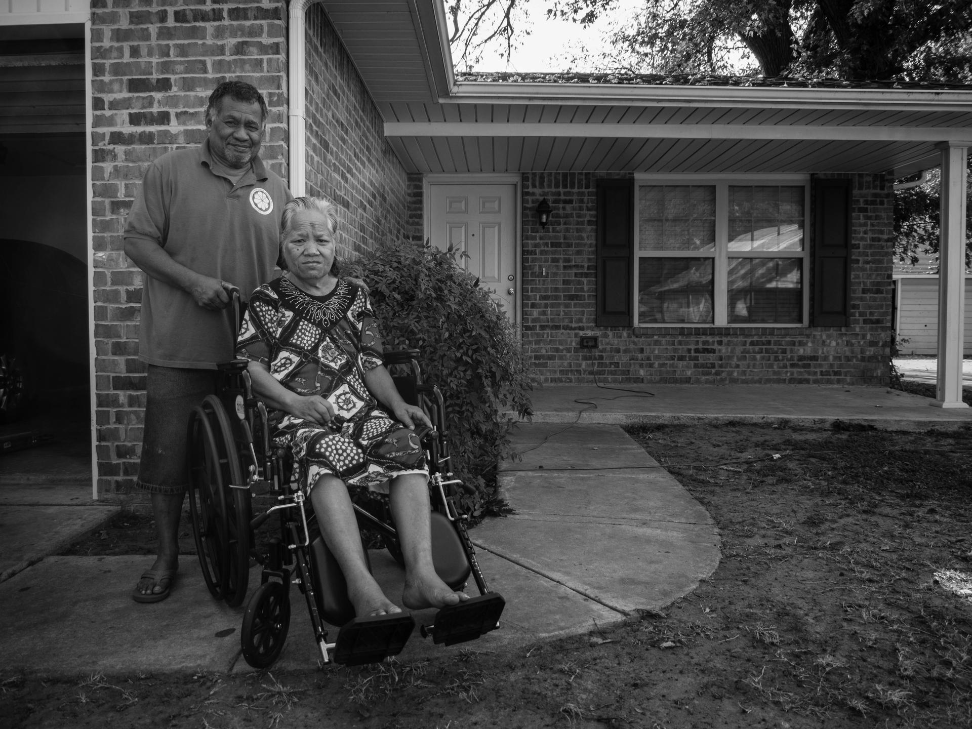 black and white photo of man and woman in wheelchair in front of house