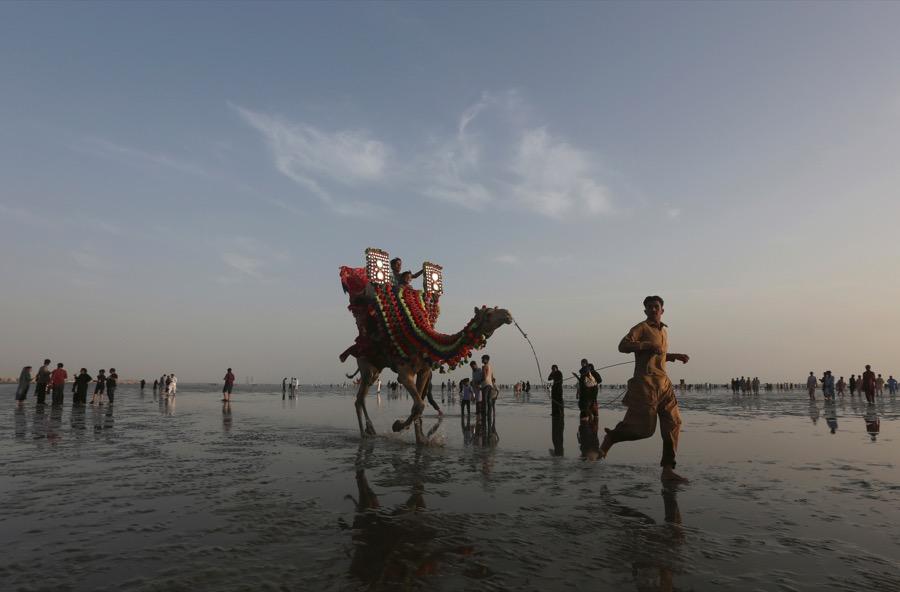 A man leads a camel with children taking a ride on it along the Clifton beach in Karachi, Pakistan 