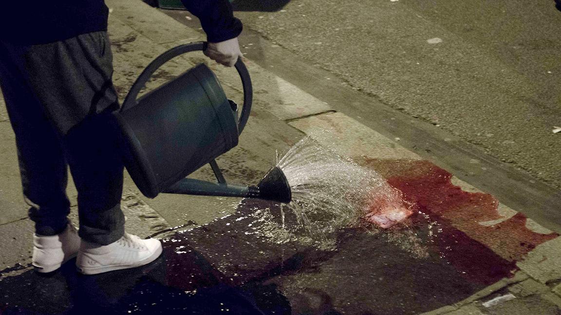 A resident washes away blood from Rue Oberkampf in the 11th district Friday night.