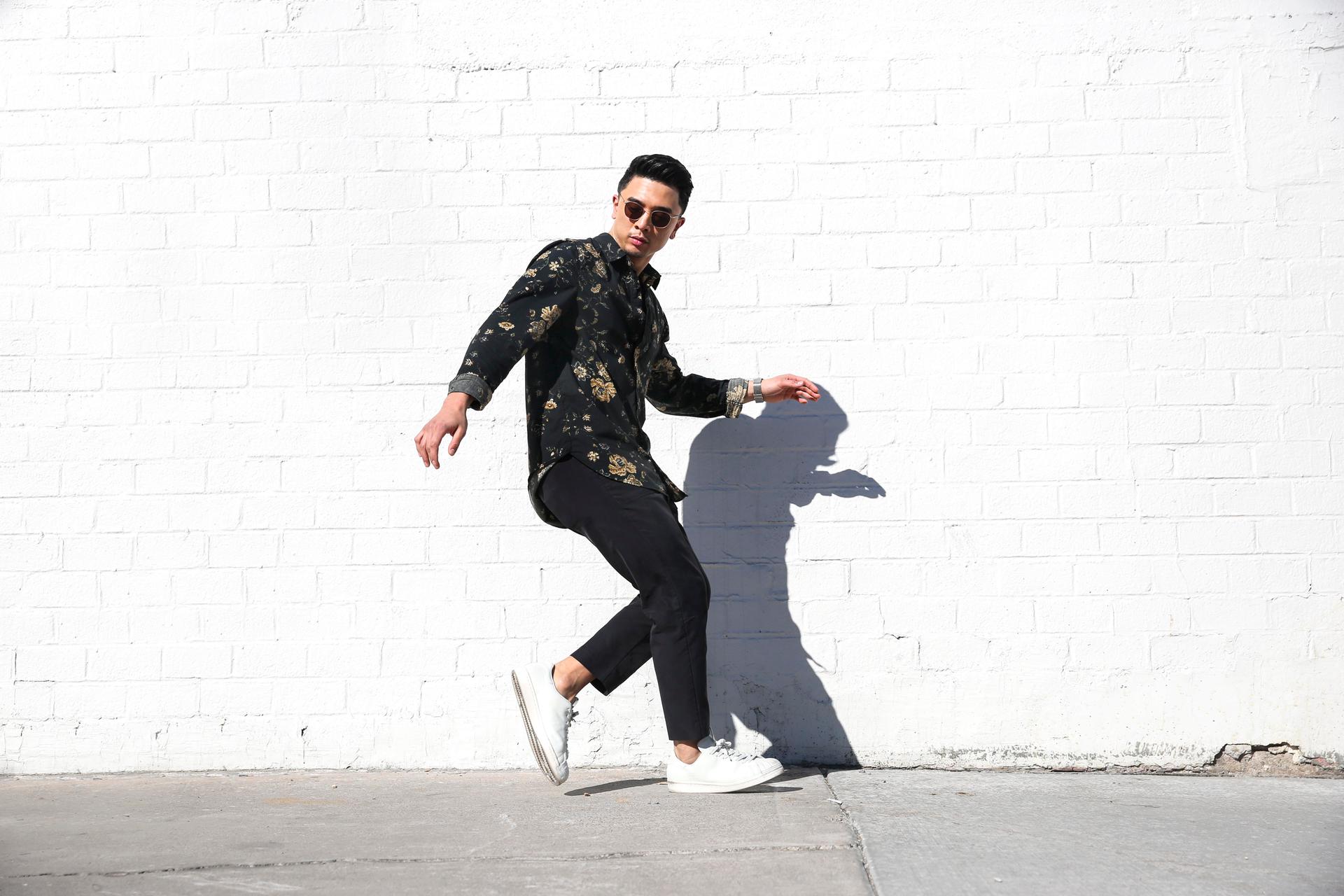 Man in sunglasses in dance pose in front of white, brick wall