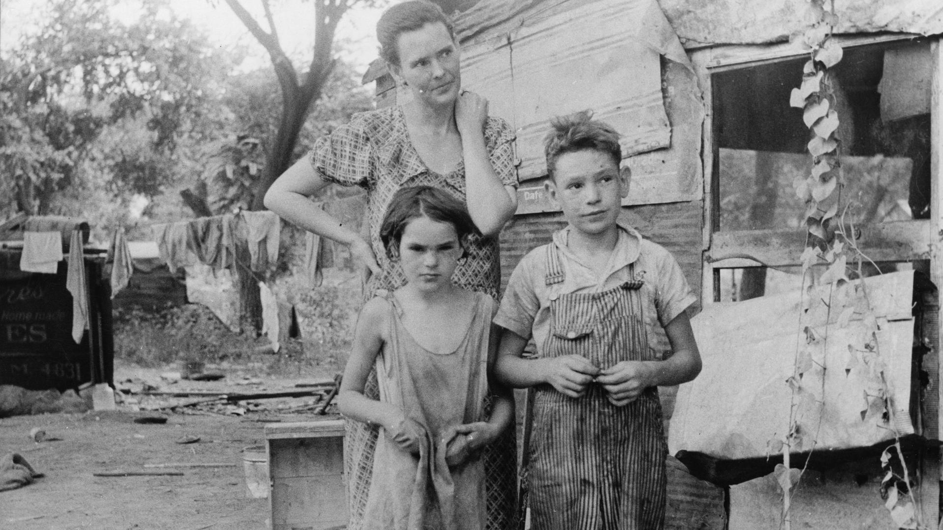The Great Depression pushed millions of Americans into catastrophic poverty. Here, a mother and her shoeless children stand beside their home, a tin shack, in Elm Grove, Oklahoma, 1st August 1936