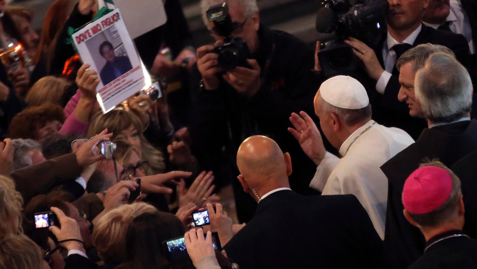 Pope Francis waves to faithful as he arrives to lead an audience with the family members of victims of the mafia at the San Gregorio VII church in Rome. A woman shows a picture of her son with the words, "Where is my son?"